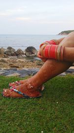 Cropped image of newlywed woman with bangles and henna tattoo sitting at sea shore