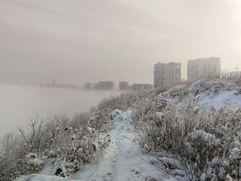 Scenic view of frozen river by buildings against sky