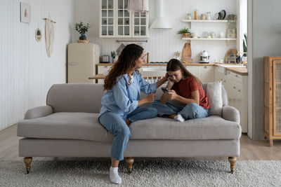 Young woman using phone while sitting on sofa at home