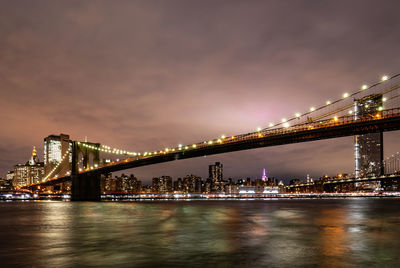 Illuminated bridge over river against sky in city at night