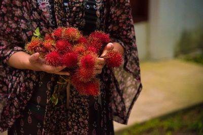 Midsection of person holding red flowering plant