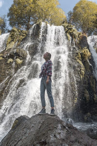 Low angle view of woman standing on rock against waterfall