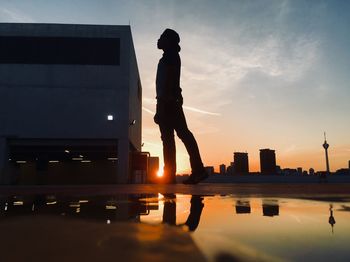 Silhouette man standing by city against sky during sunset