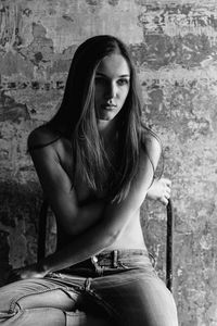 Shirtless young woman sitting on chair against wall