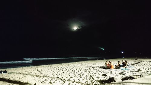 People enjoying at beach against sky at night