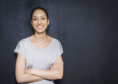 Portrait of smiling young businesswoman standing arms crossed against wall