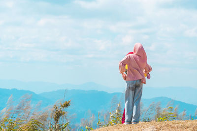 Rear view of man standing on mountain against sky