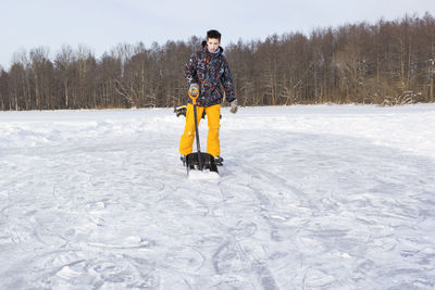 Full length portrait of teenage boy cleaning snow on land