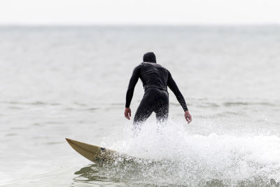 Rear view of man surfboarding in sea against sky