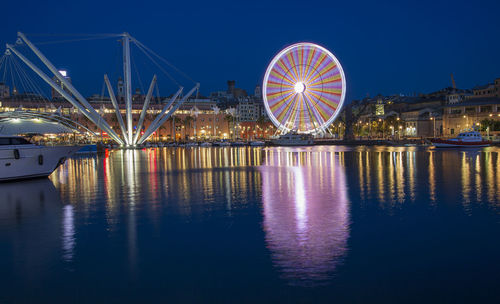 Illuminated ferris wheel by river against sky at night