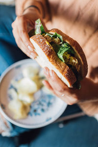 Woman holding tuna salad sandwich with plate of potato chips on her lap