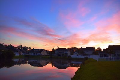 Lake by houses against sky during sunset