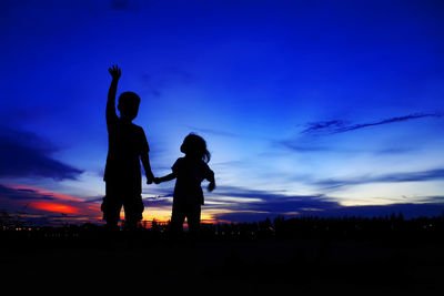 Silhouette siblings standing against dramatic sky