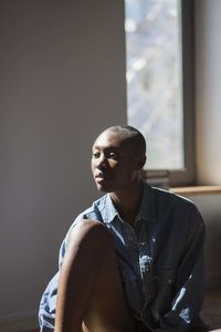 Young man looking away while sitting on window