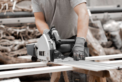 A young man is sawing a board with an electric saw.