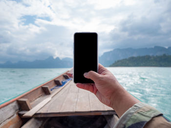 Man using mobile phone in sea against sky