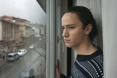 Portrait of young man looking through window