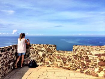 Rear view of couple standing on retaining wall against sea