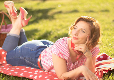 A woman dressed in pin-up style lies on her stomach on a red blanket. red heels, blurred background.