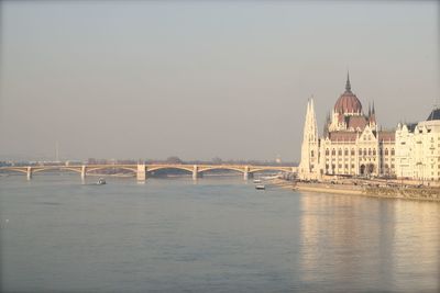 Hungarian parliament building by danube river against sky