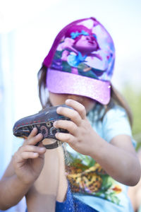 Close-up of girl holding shoe while sitting against sky