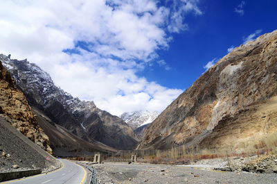 Country road by mountains against sky