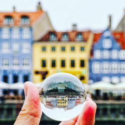 Close-up of hand holding glass against buildings in city