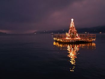 Illuminated christmas tree by sea against sky at night