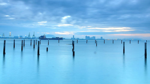 Wooden posts in sea against sky during winter