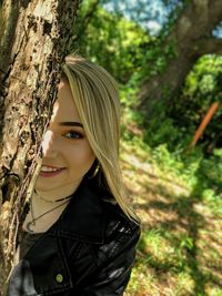 Portrait of smiling young woman against tree trunk