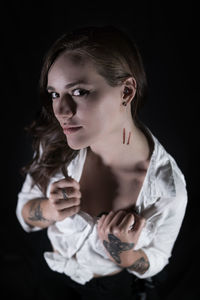 Portrait of young woman showing wounds on neck against black background