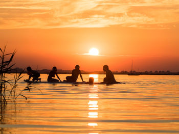 Silhouette of people sitting on surfboard at sunset