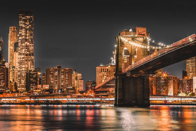 Illuminated buildings by river against sky at night