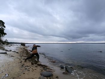 Rear view of man standing at beach against cloudy sky