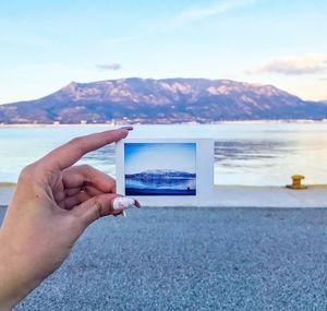 Cropped hand of woman holding photograph against lake