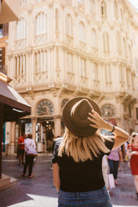 Back view of adventurous traveler touching her hat visiting majorca