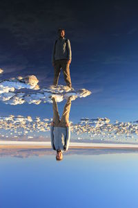 Reflection of man standing on snow in lake against clear blue sky