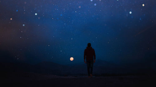 Rear view of man walking against sky at night