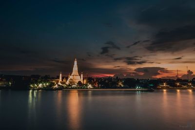 Wat arun in illuminated city against sky at sunset