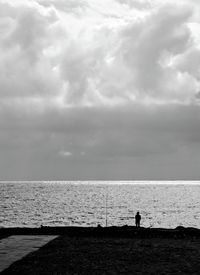 Silhouette of people looking at sea against sky