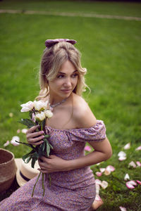 Portrait of a beautiful young woman sitting on a green meadow in summer and holding a bouquet 