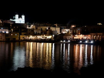 Illuminated buildings by sea against clear sky at night