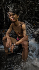 Young man looking away while sitting on rock