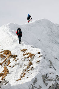 Low angle view of mountaineers climbing snowcapped mountain against sky