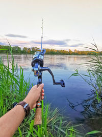 Man holding fishing rod by lake against sky