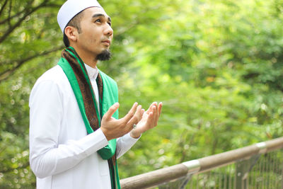 Mid adult man praying while standing by railing at park