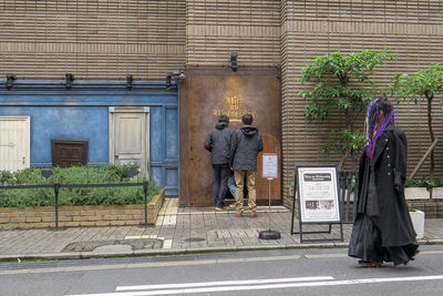 Rear view of people walking on footpath against building