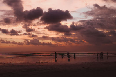 Silhouette people on beach against sky during sunset