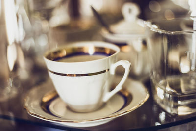 Close-up of cup and saucer by drinking glass on table