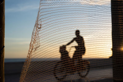 Silhouette of cyclists and people walking on the edge of a beach against sunset. 